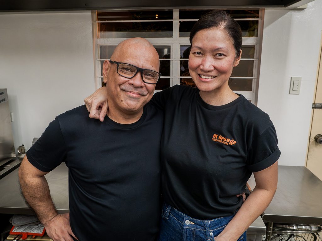 Chef Nats and Ethel smiling in the kitchen wearing 61 Orange branded shirts